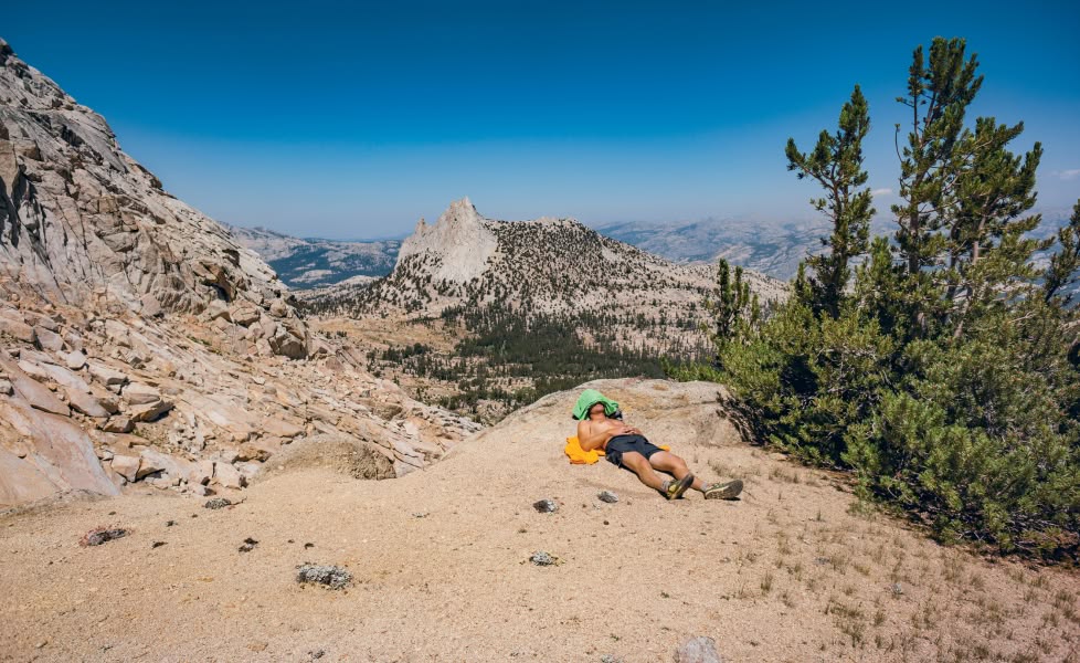 A person takes a break from a trail run by lying in the dirt by a tree.