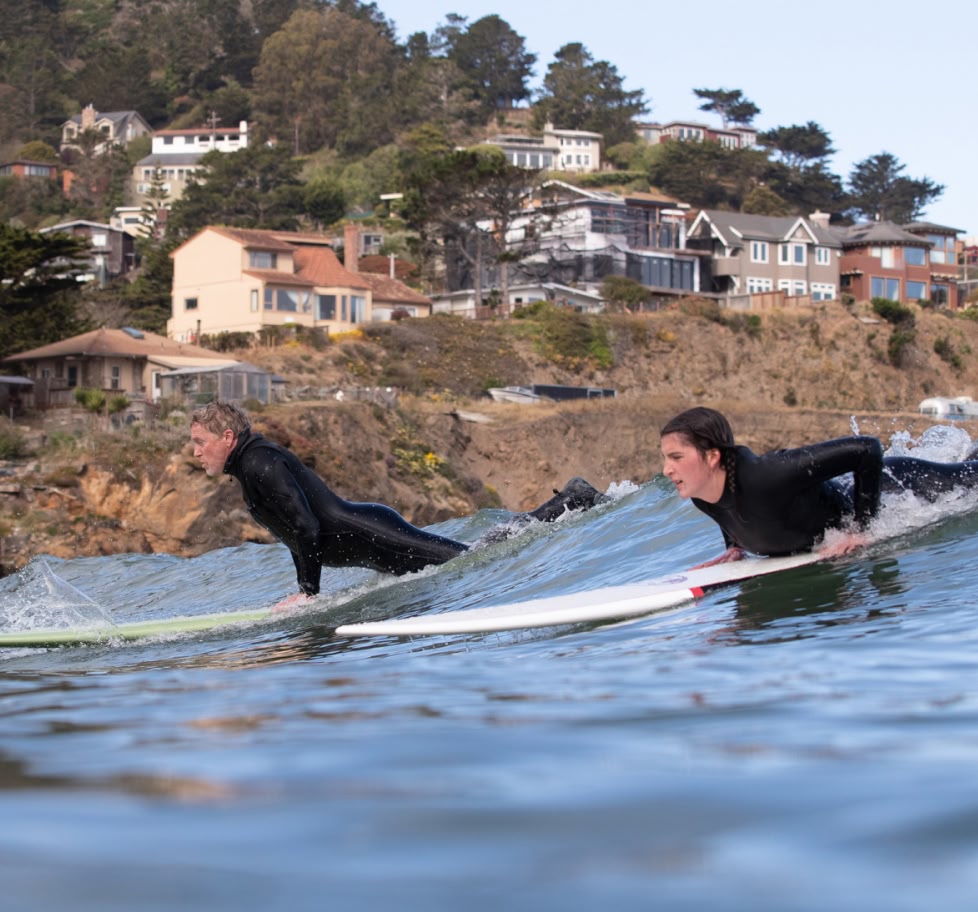 Two surfers prepare to hop up on their boards while sharing a wave.