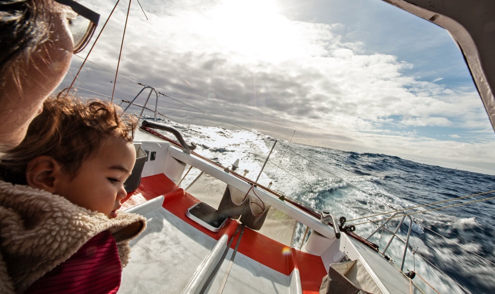A person sits with a small child on a boat on the high seas.