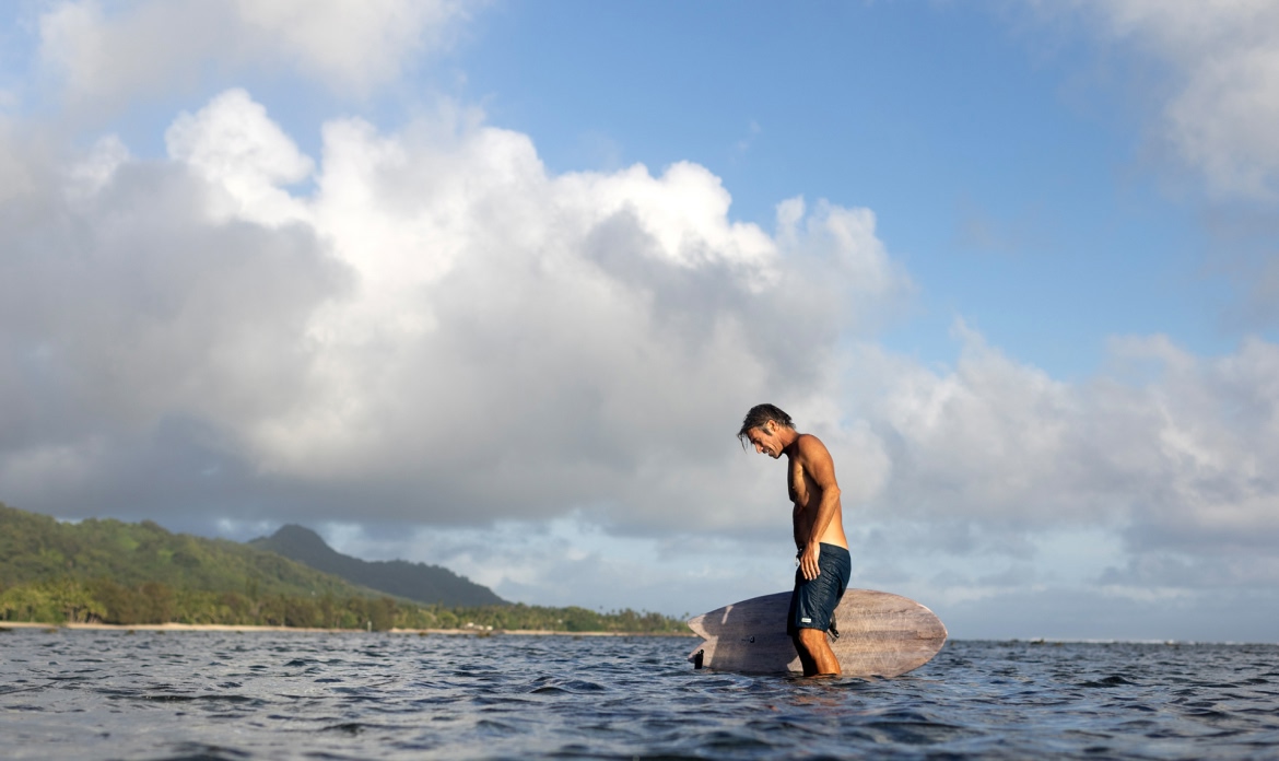 A surfer walks through shallow water back to the beach.
