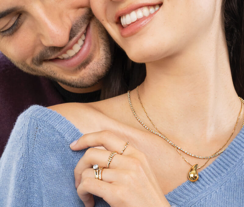 A smiling couple pose, showcasing beautiful Gold Anniversary Rings and Gold Necklaces.