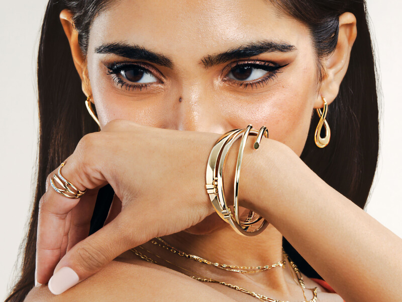 A woman poses, showcasing stunning Gold Bracelets, Earrings and Rings