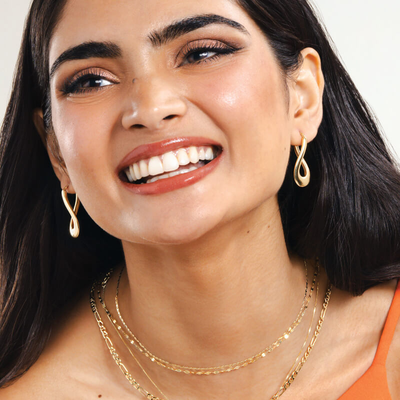 A woman poses, showcasing stunning Gold Neclaces and Earrings.