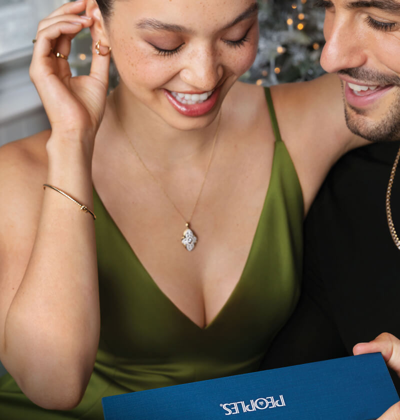 A smiling couple pose, excited to open a PEOPLES gift box.