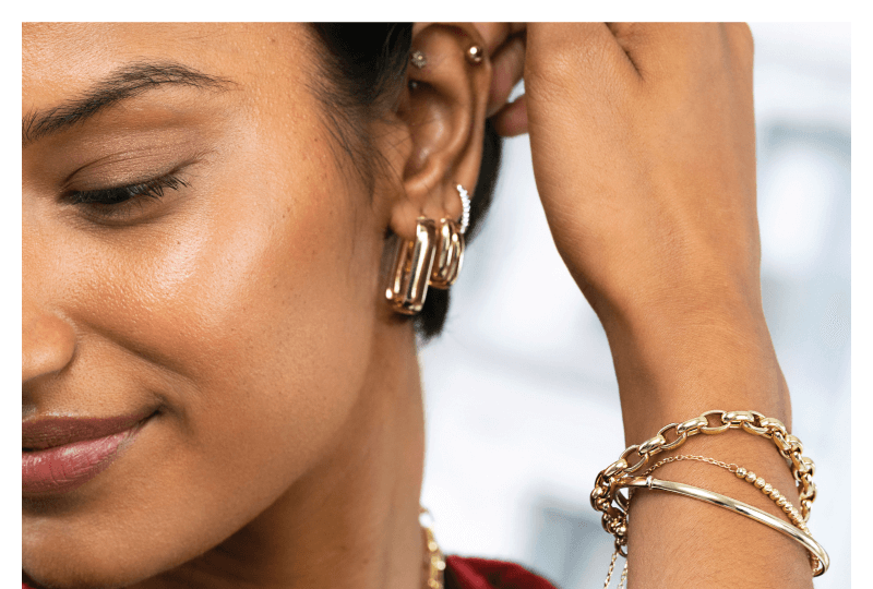Woman showcasing elegant bracelets and earrings in gold.