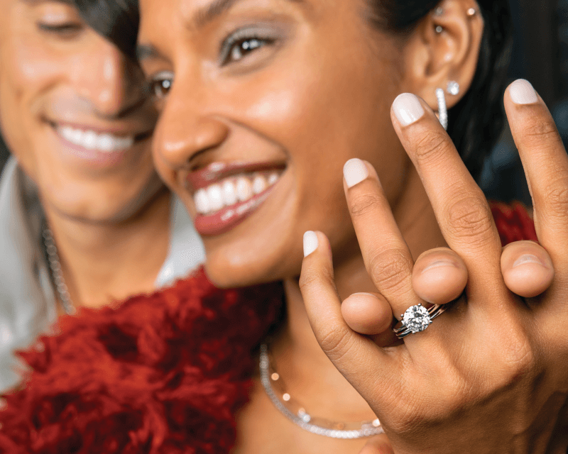Smiling woman showing off a large diamond engagement ring while standing close to her partner.