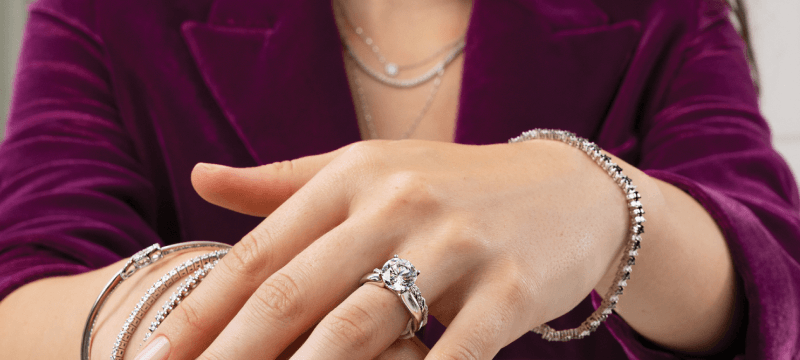 Close-up of model’s hands wearing stacked diamond rings and bracelets over a deep purple blazer.
