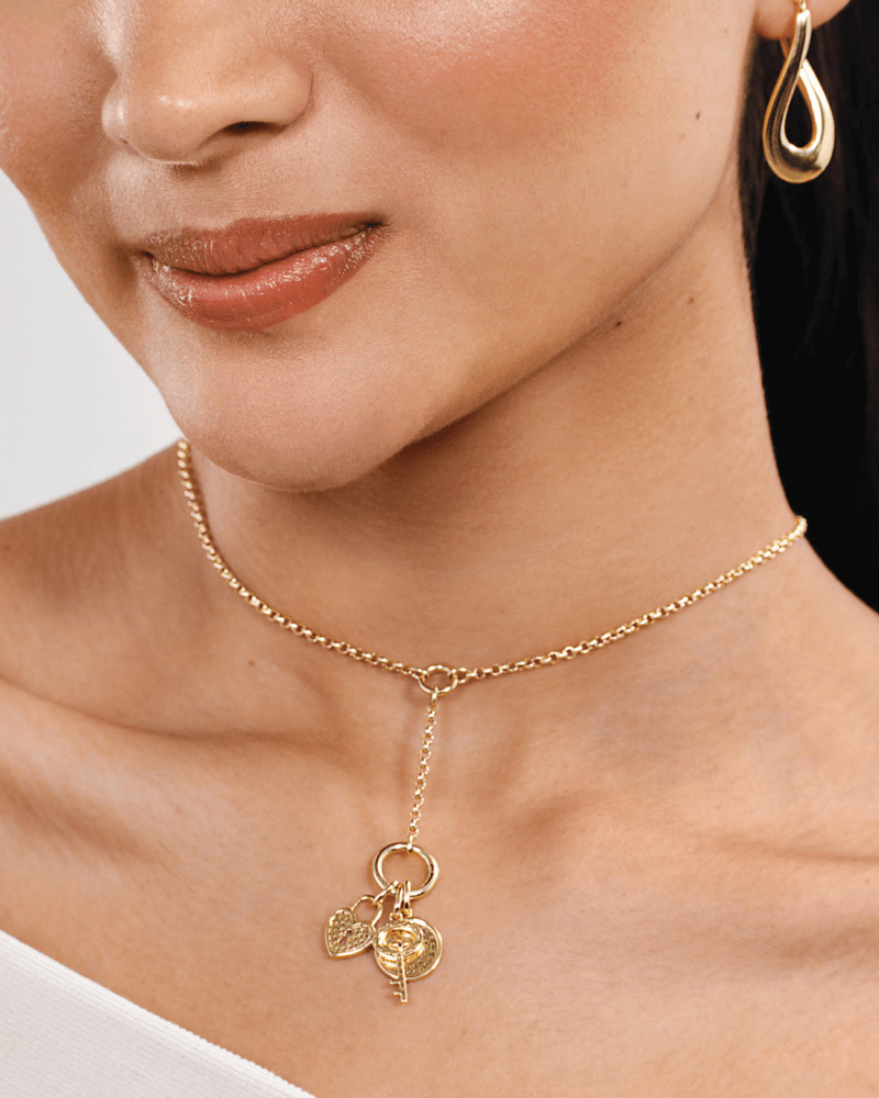 Woman wearing a gold teardrop earring and a delicate gold Y-necklace with small charm pendants resting at the collarbone.