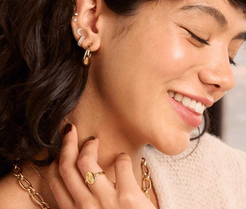 Close up of a model wearing stacked gold earrings, gold chain necklace, and gold ring.