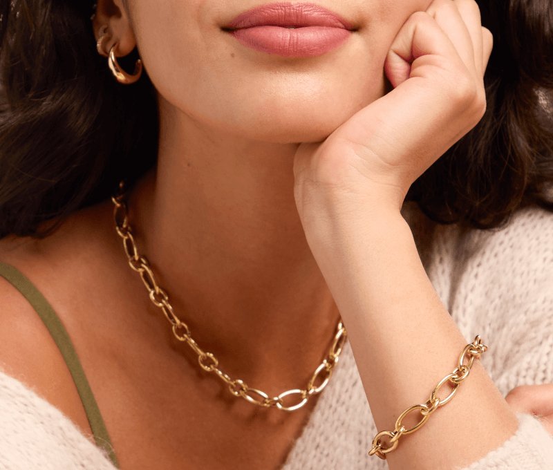 Woman wearing stacked yellow gold hoop earrings, yellow gold chain link necklace, and matching chain link bracelet.