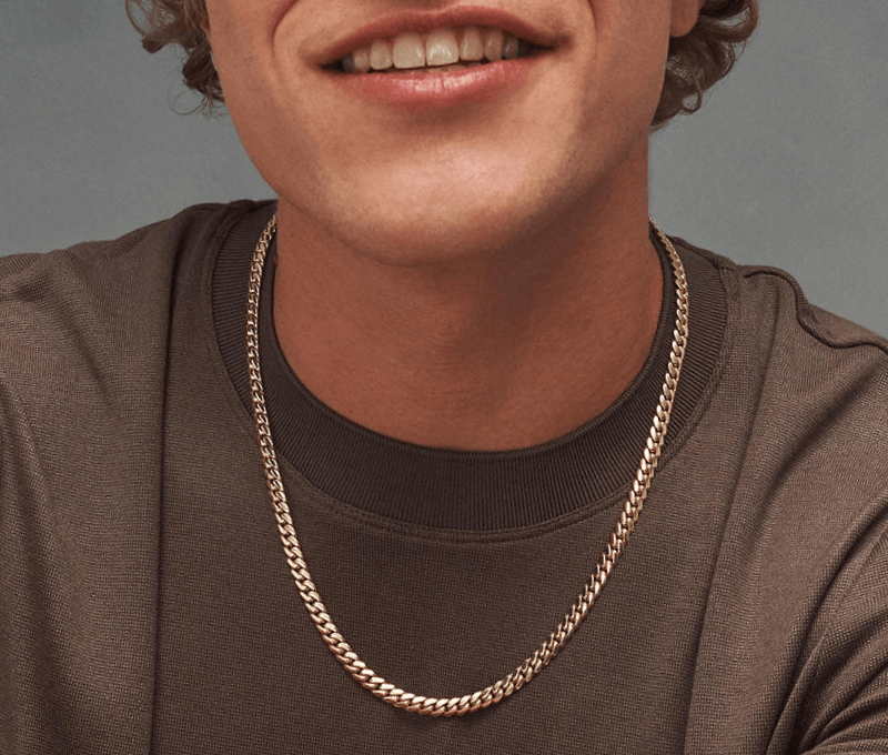Man wearing brown shirt and gold chain link necklace, and woman in blue top wearing layered gold necklaces and gold earrings.