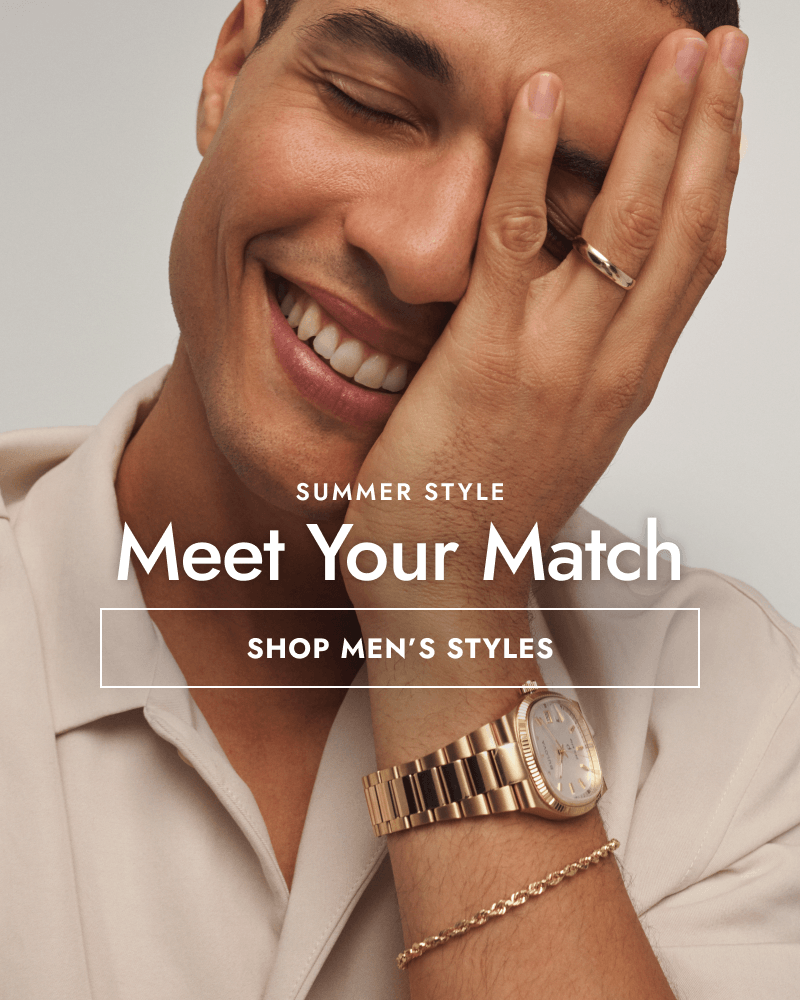 Smiling man with hand on his face wearing gold watch, bracelet and ring. Summer style: meet your match. Click shop men’s styles.