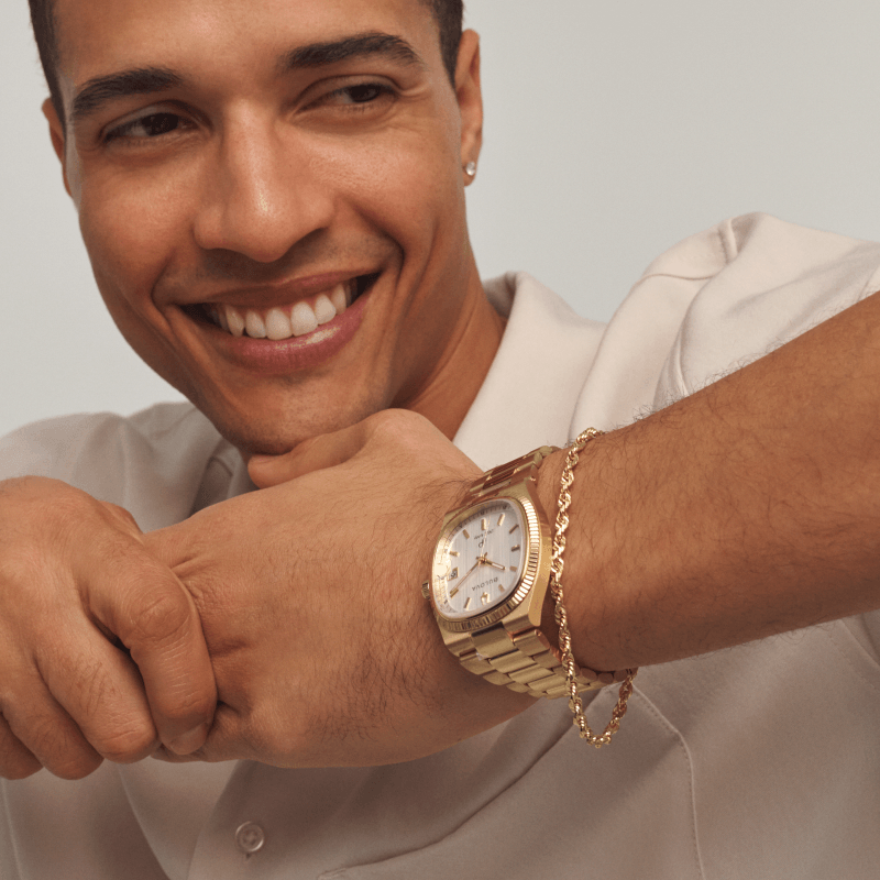 Smiling man wearing gold watch, bracelet and ring. 