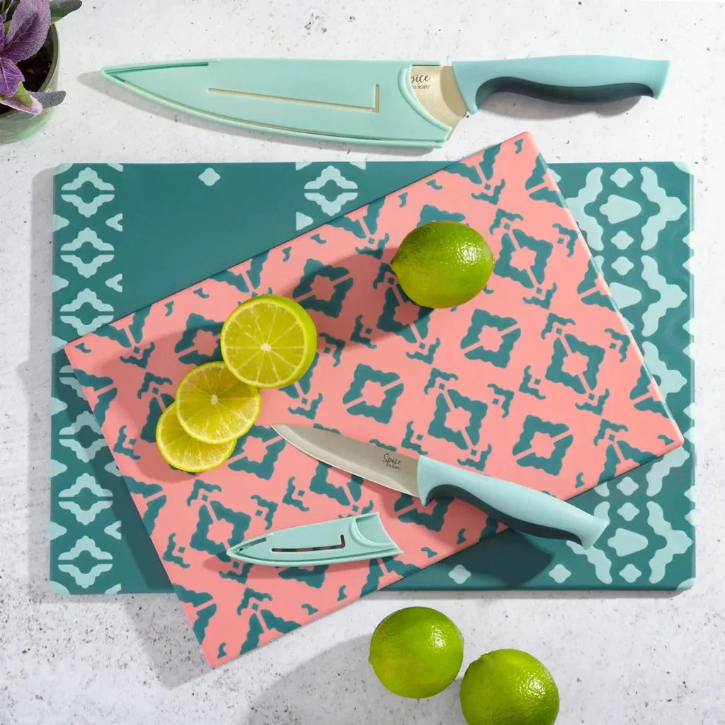 Colorful kitchen knives and cutting board set with sliced limes on patterned surface, styled flat lay.