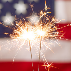 Two sparklers glowing bright in front of an American flag.