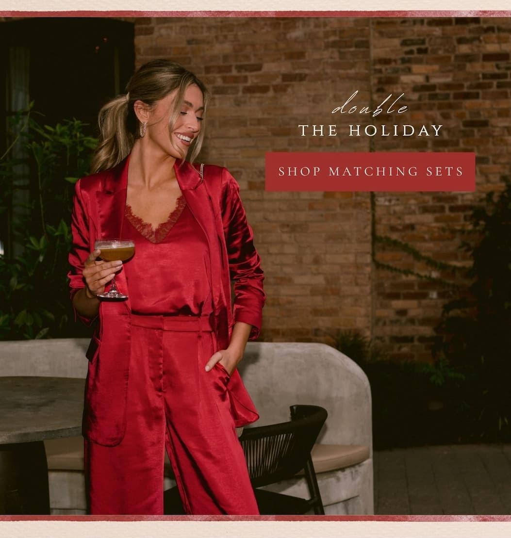 'Double the holiday.' Image of model wearing a red satin top with a matching blazer and pants. Button: 'Shop Matching Sets.'