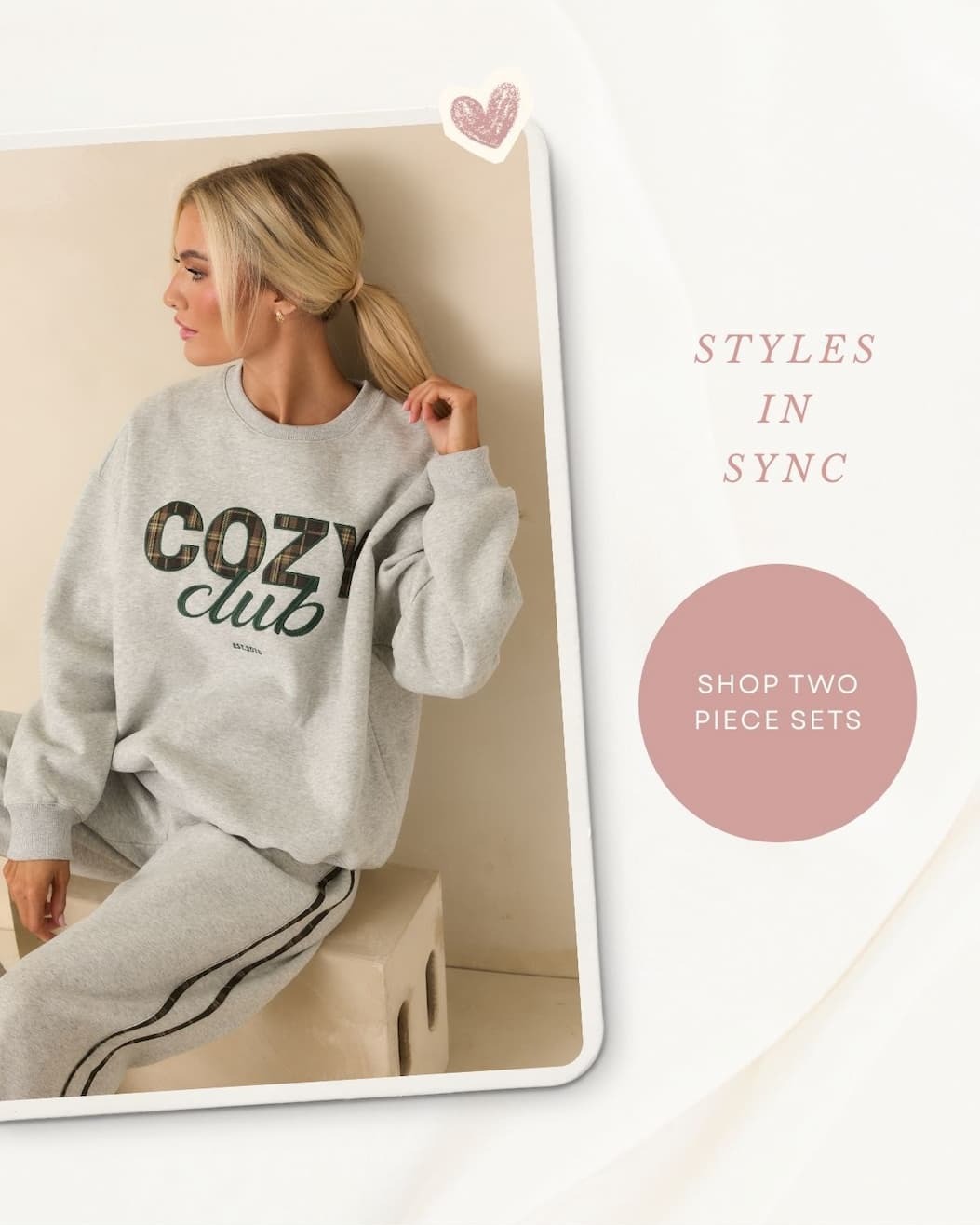 Image of model wearing a Cozy Club Heather Grey Crewneck Sweatshirt with matching sweat pants. 'Styles in sync.' Button: 'Shop two piece sets.'