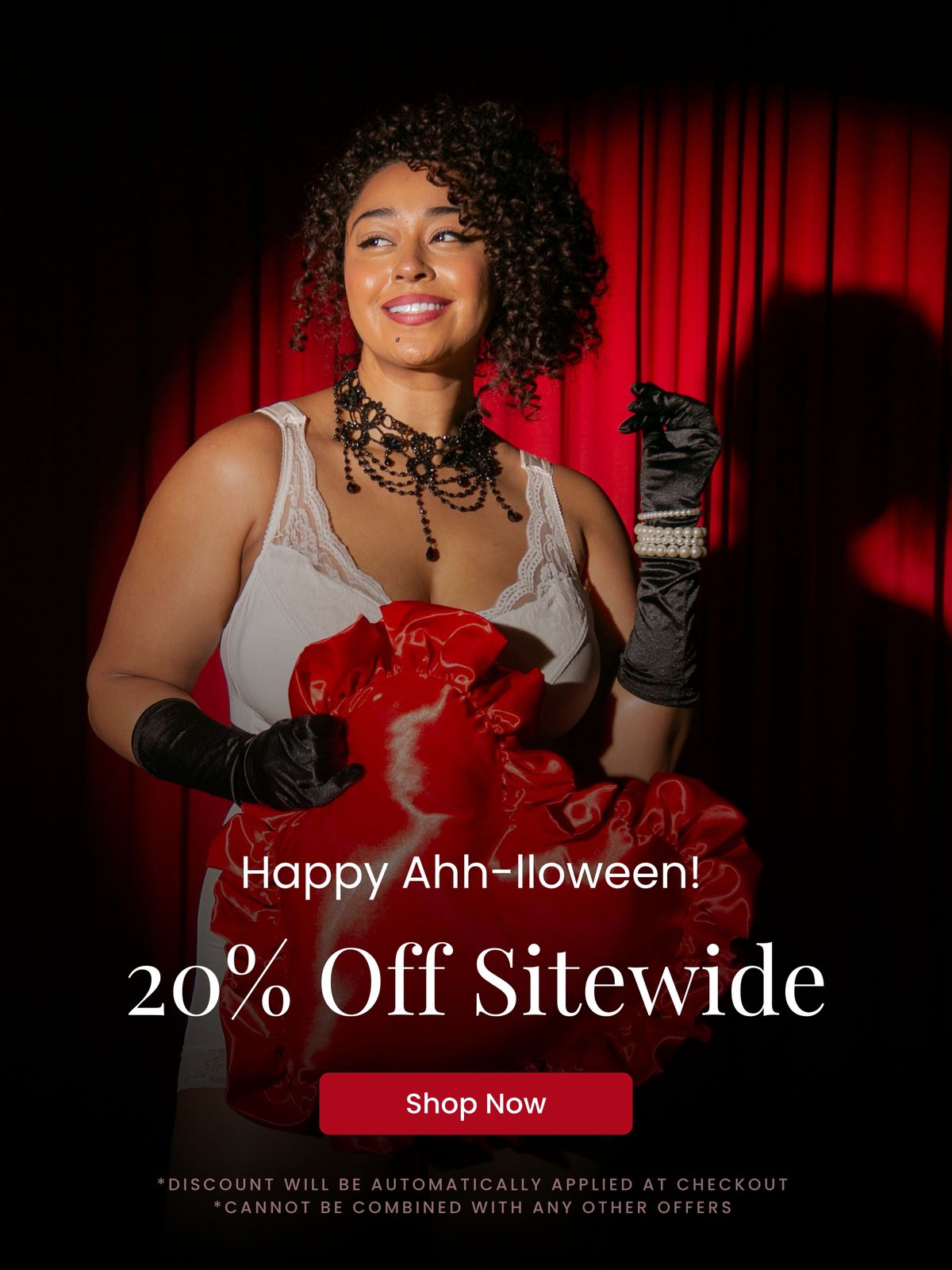 Model in glamorous lingerie posing in front of red stage curtains, promoting Rhonda Shear’s Happy Ahh-loween sale with 20% off sitewide.