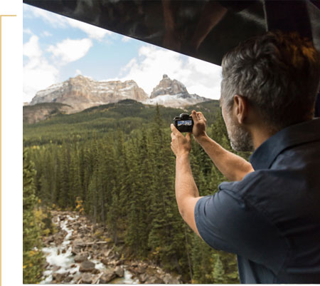 Guest taking a photo of mountains from the outdoor viewing platform onboard Rocky Mountaineer.