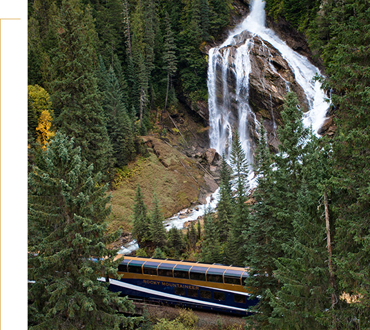 Rocky Mountaineer train travelling across a river with Pyramid Falls above.