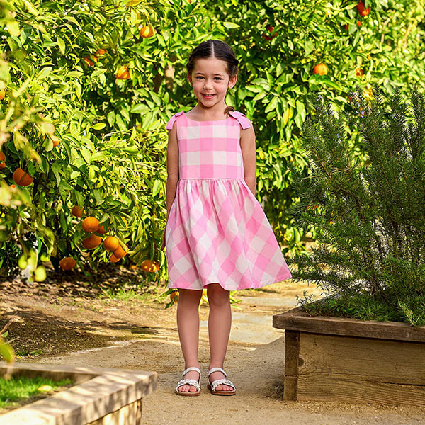 Girl wearing pink gingham dress in garden. 