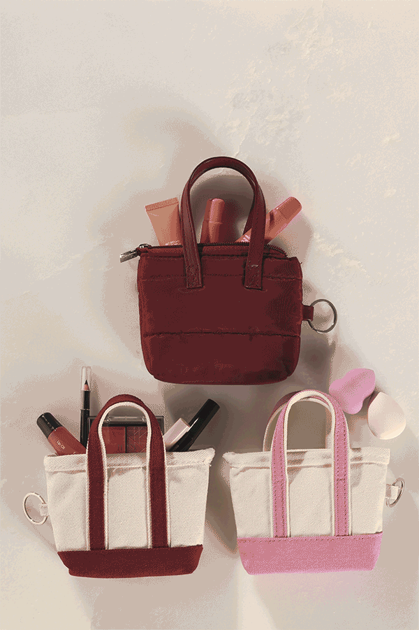 Three mini totes with mini beauty products inside, hand picking out a lip gloss from the mini tote. 
