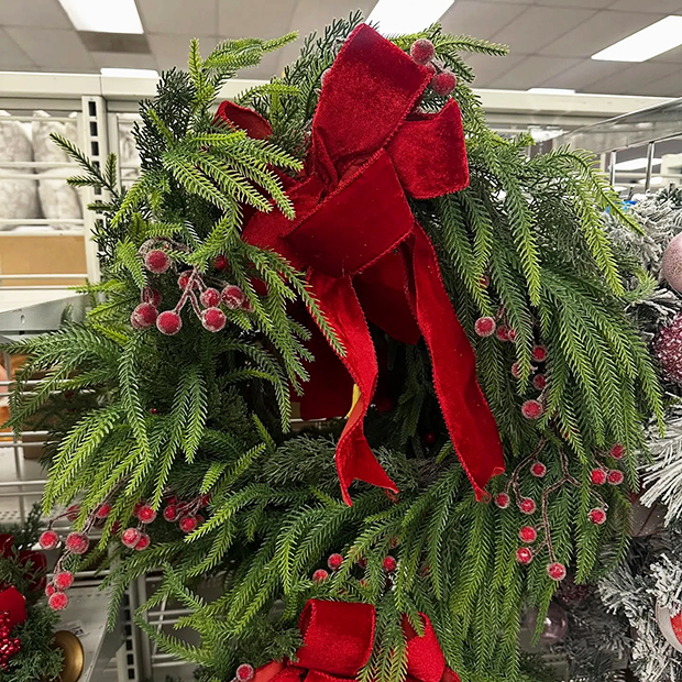 Festive holiday wreath made of green pine branches, decorated with red berries and a large red velvet bow.