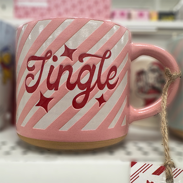 A pink ceramic mug with diagonal white stripes and red lettering that reads “Jingle,” accented with star designs. 
