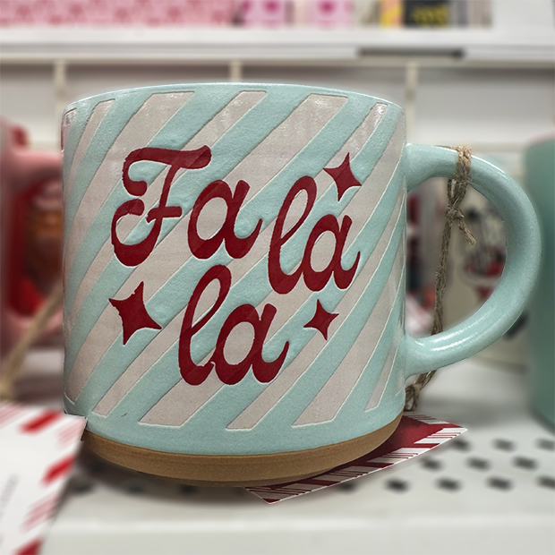 A light blue ceramic mug with diagonal white stripes and red lettering that reads “Fa la la,” accented with small star designs. 