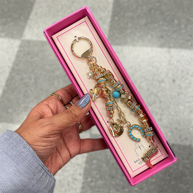 Colorful gold-tone bag charm with turquoise accents and multiple charms, displayed in a pink gift box. 