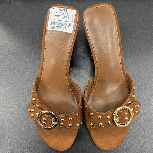 Brown suede slide sandals featuring a wide strap with gold studs, round gold buckle detail, and cushioned footbeds. 