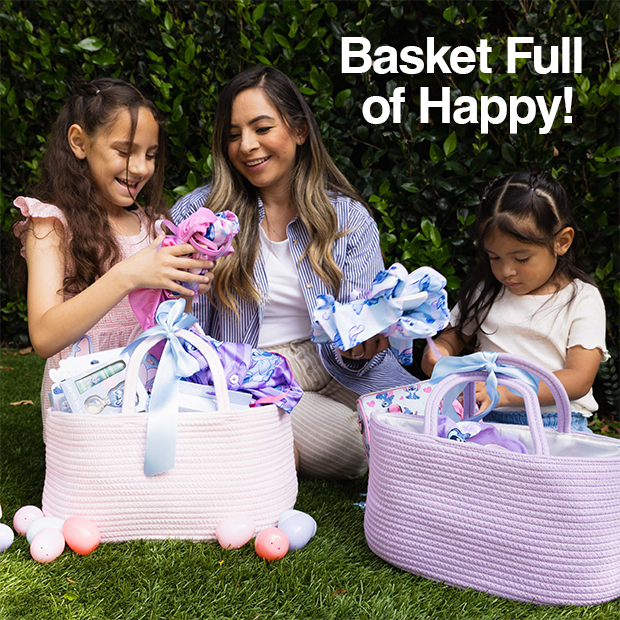 Adult and two children sitting on grass with large pastel Easter baskets filled with gifts and wrapped items.