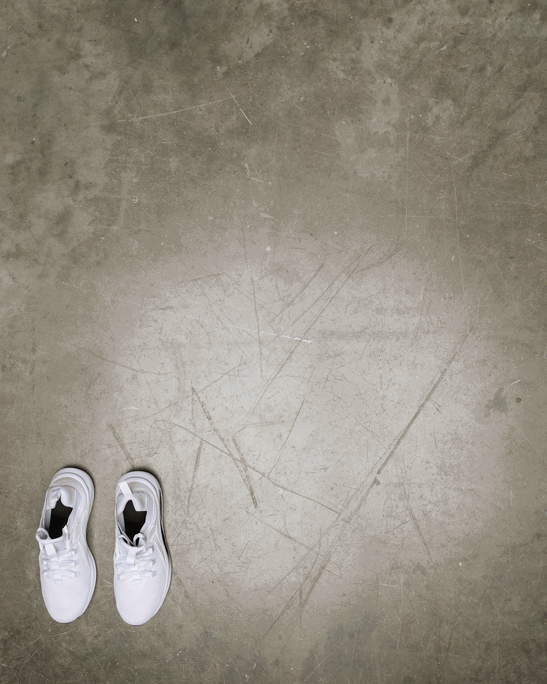Pair of white sneakers and sporty mens gear placed on a textured concrete floor with ample negative space.
