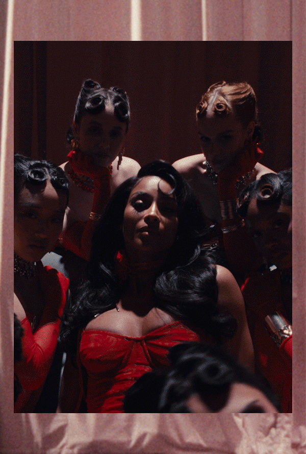 Ciara and group in coordinated red outfits posing in a dramatic studio setting with soft draped backdrop and stylized lighting.