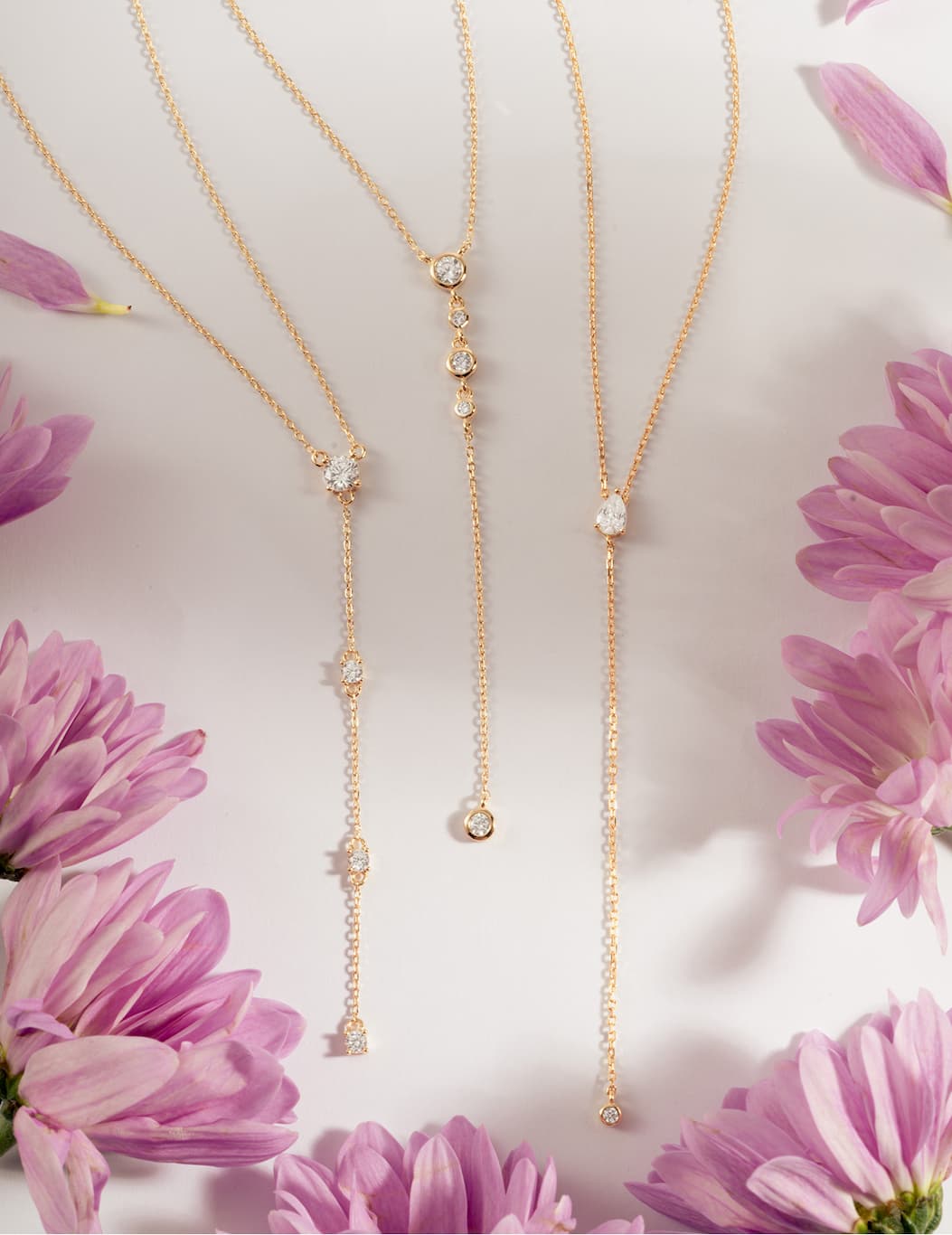 Three gold lariat necklaces with CZ stones styled among pink flowers