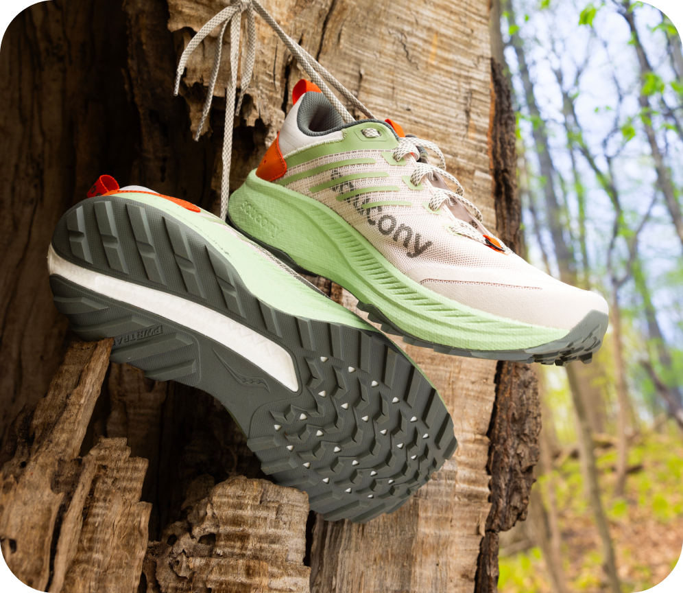 [saucony] Close image of green and white Saucony Trail shoes hanging on a tree