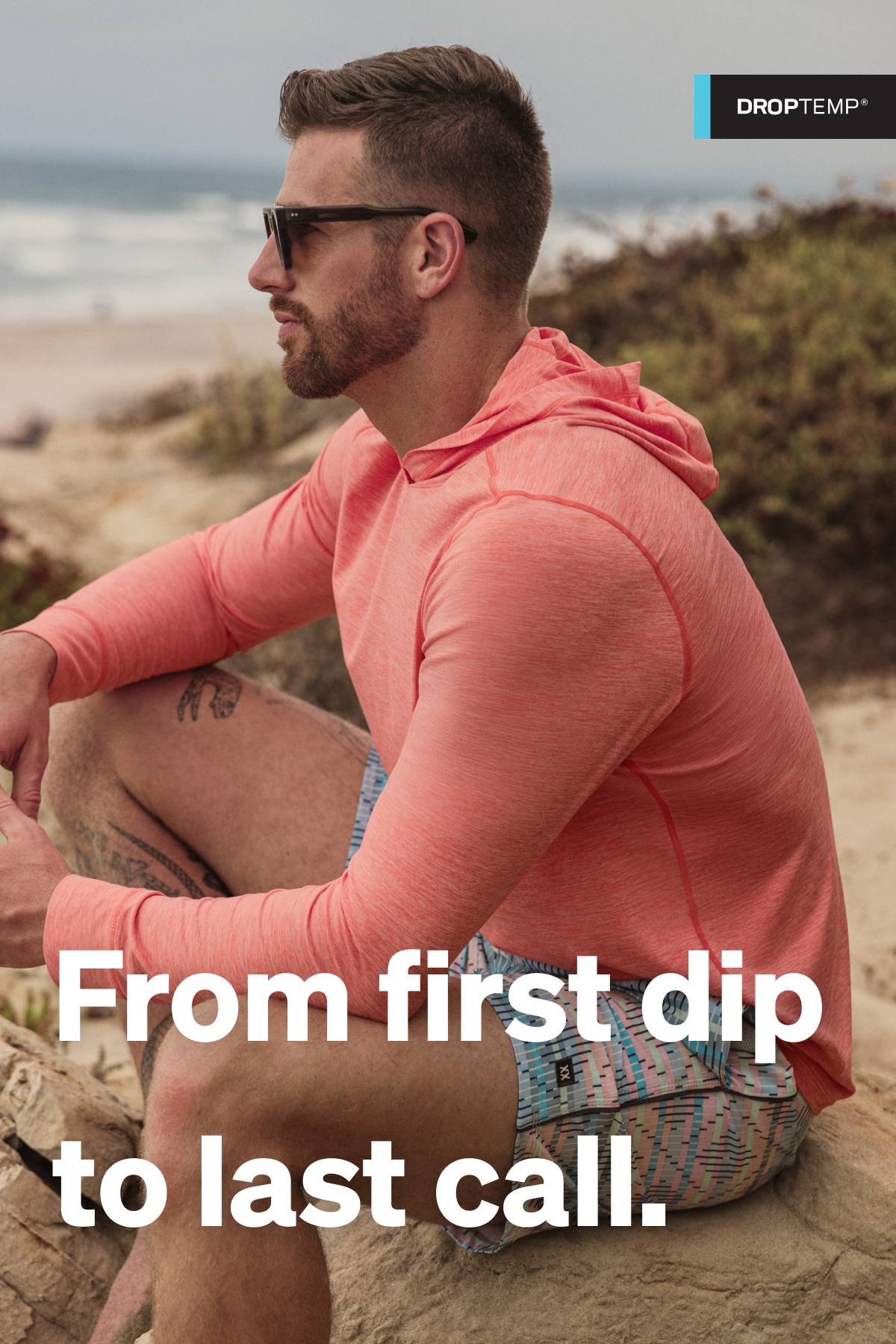 Man wearing a coral SAXX performance hoodie sitting on a beach, with “From first dip to last call” text overlay.
