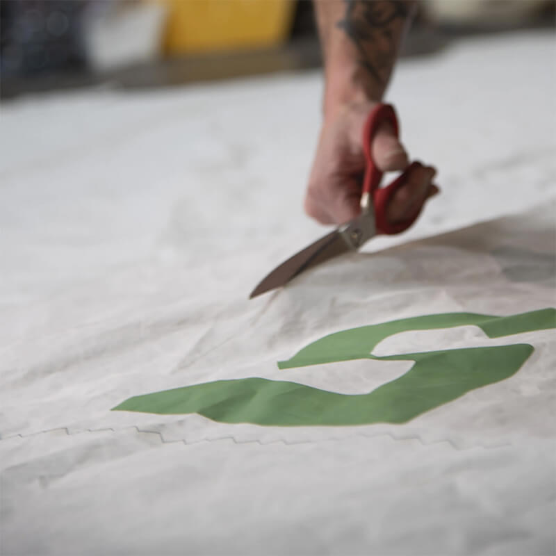 A person cutting sail fabric with a green insignia