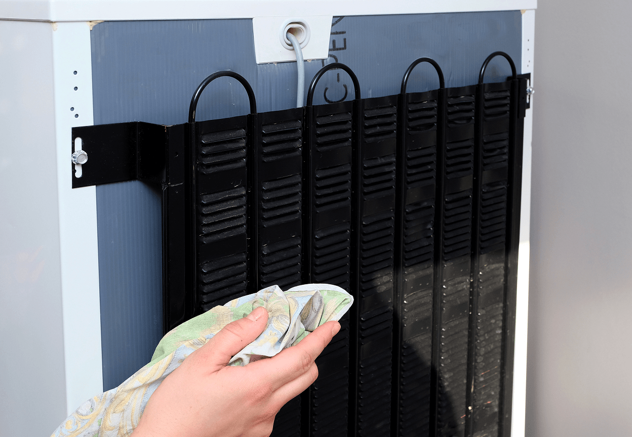 A person cleaning the back coils of a refrigerator