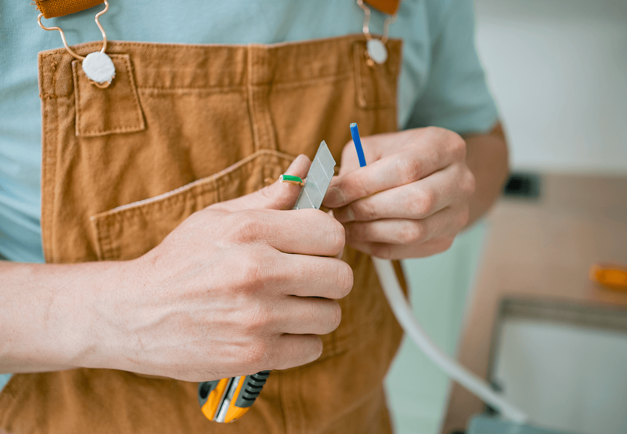 A person stripping the plastic sheathe from a copper wire