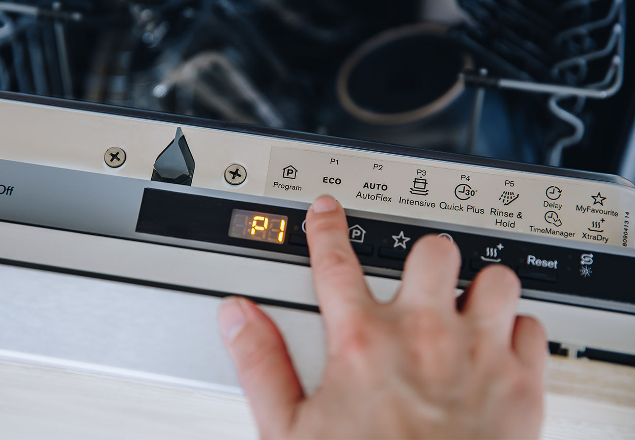A person selecting a dishwasher cycle on a dishwasher door
