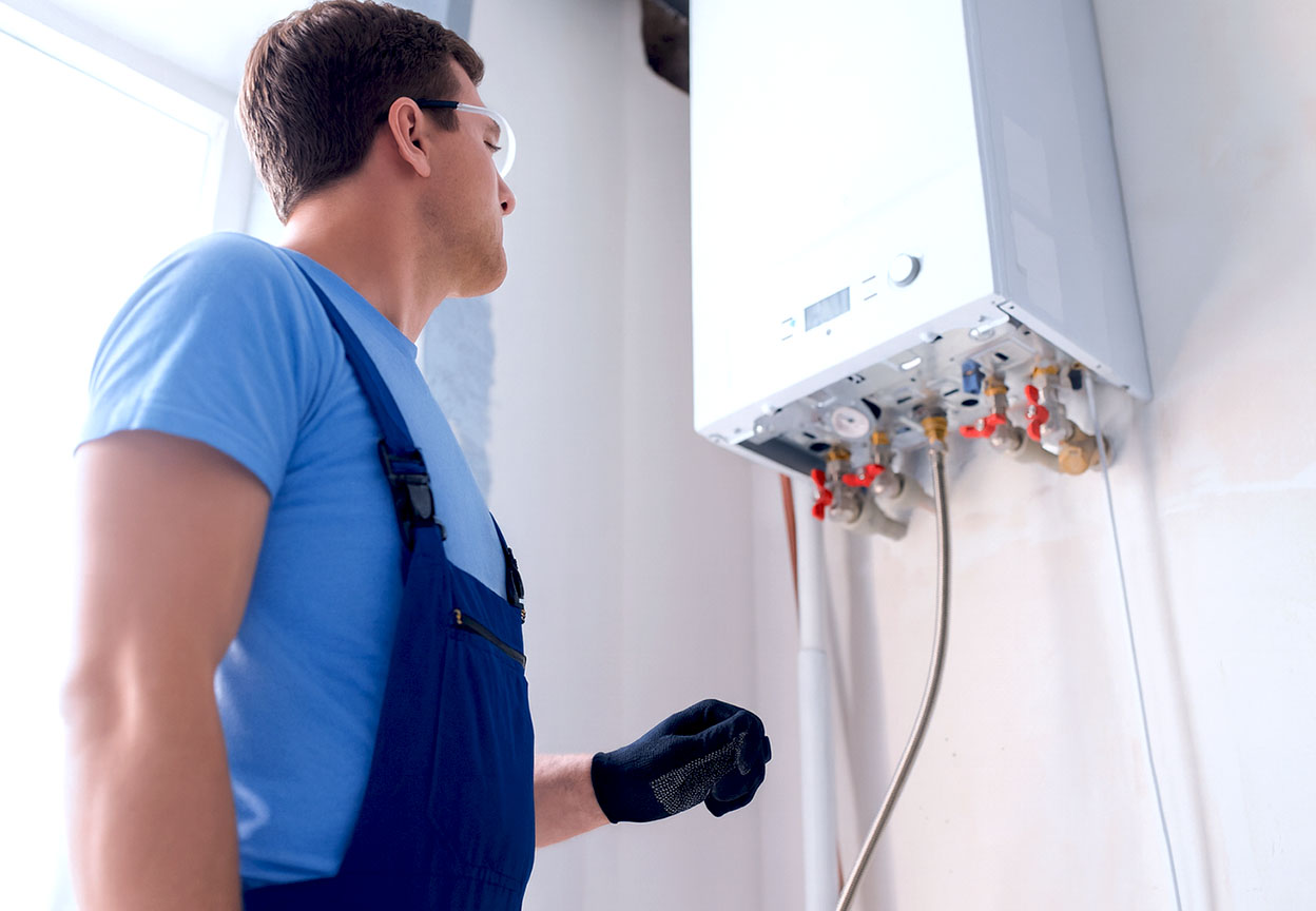 Technician in blue overalls inspecting a modern wall-mounted boiler in a bright utility room
