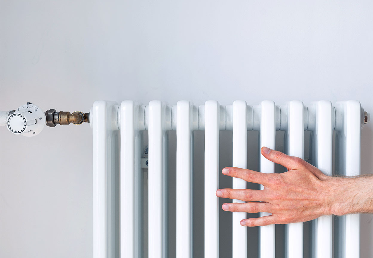 A person’s hand resting on a white home radiator to check the heat