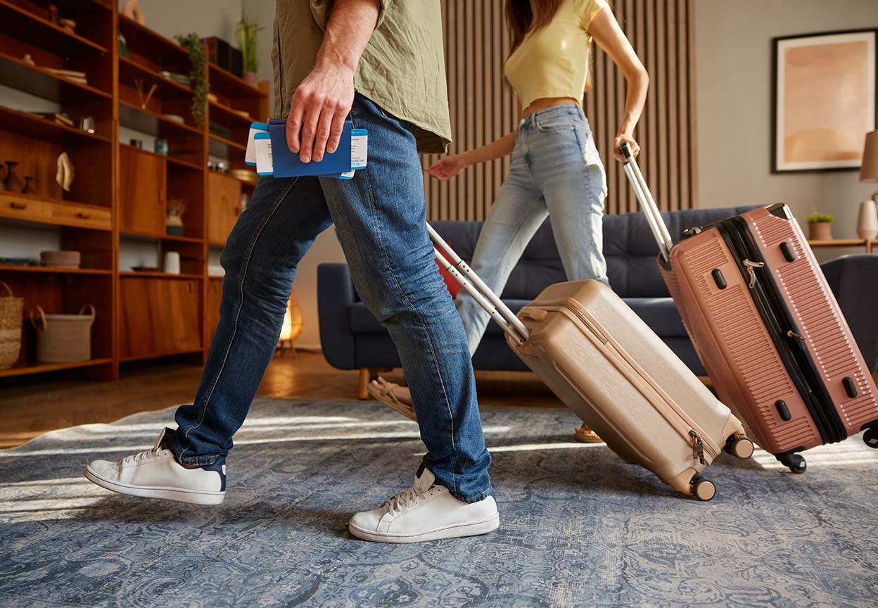 Couple walking through their living room with rolling suitcases and boarding passes, getting ready to travel