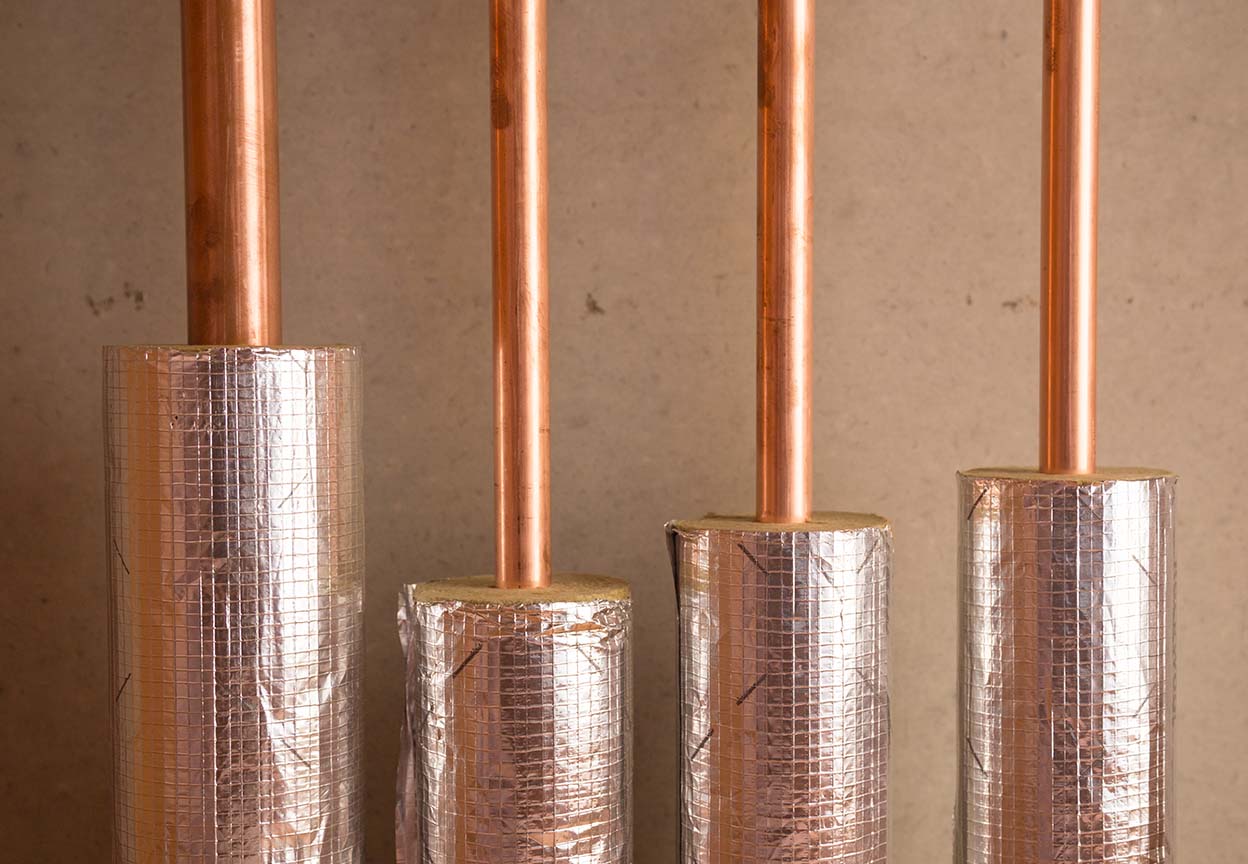 Close up of copper pipes wrapped with shiny insulation to protect them from heat loss and freezing