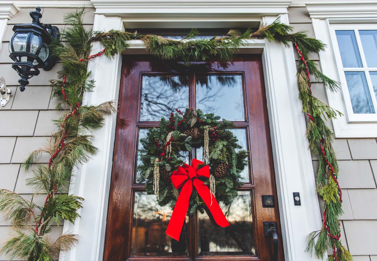 Front door decorated with a holiday wreath and garland, featuring a bright red bow to welcome guests