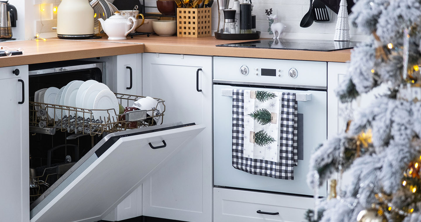 Holiday kitchen with an open dishwasher full of clean dishes, a decorated oven, and a lit Christmas tree