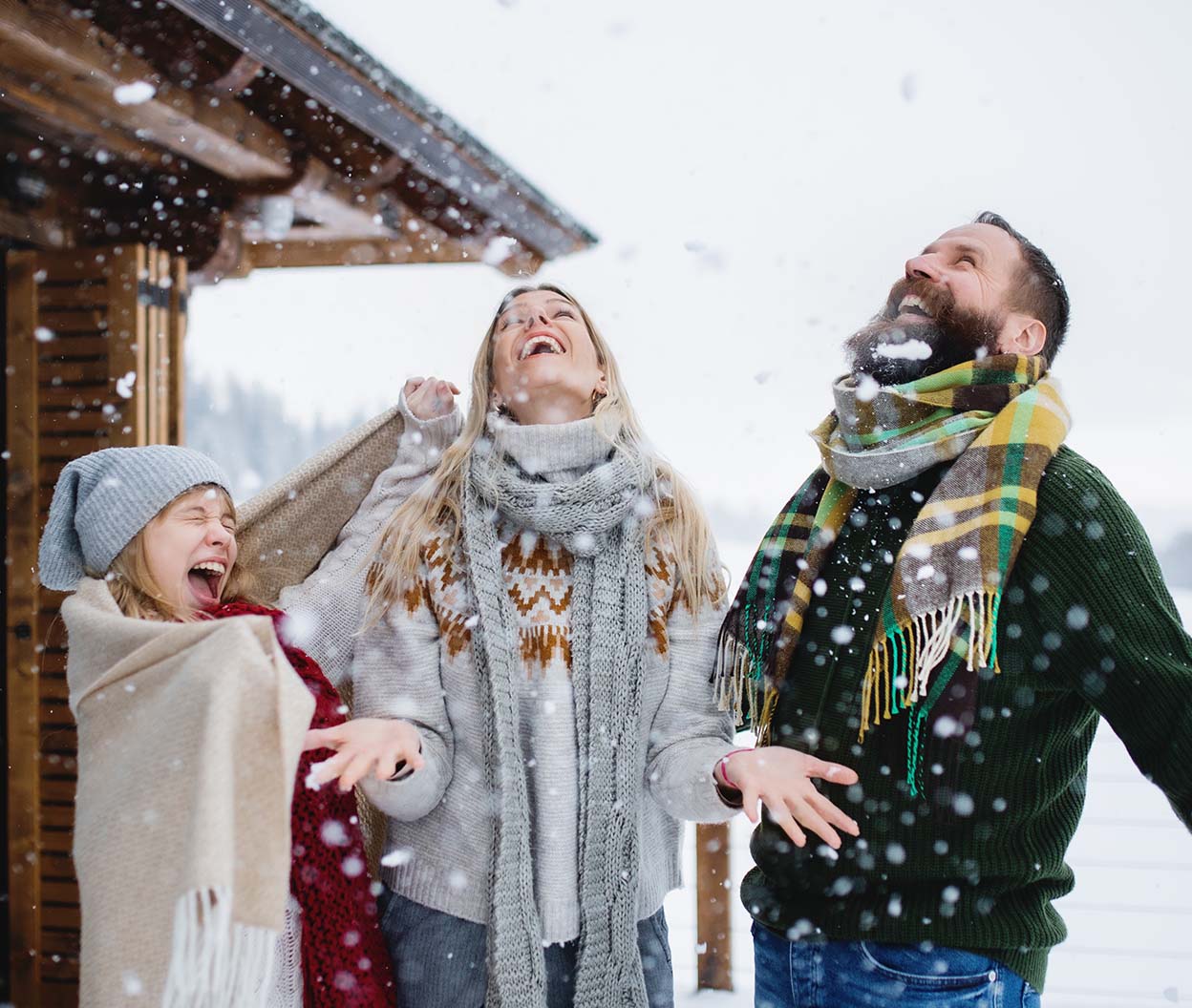 A family bundled in winter clothing laughs joyfully as snow falls around them