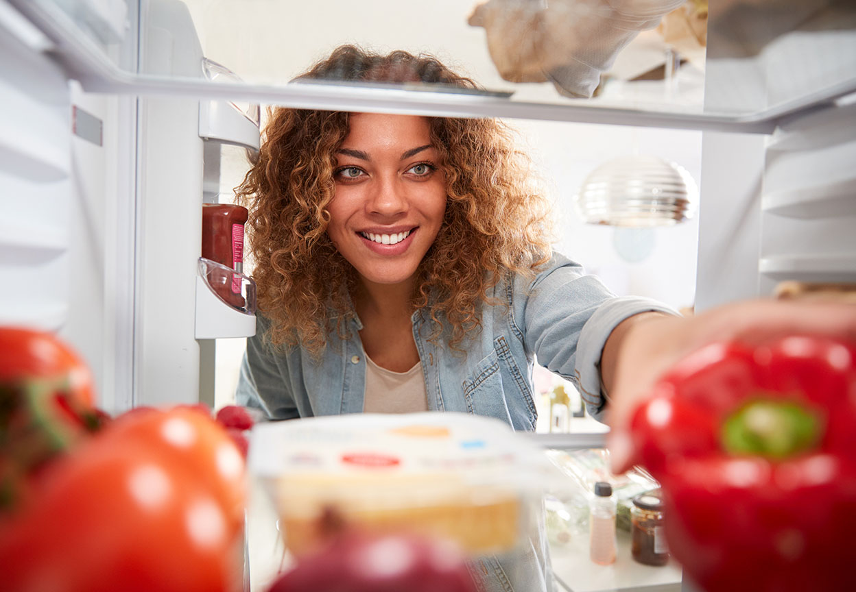 View from inside a refrigerator as a woman reaches in to grab fresh food