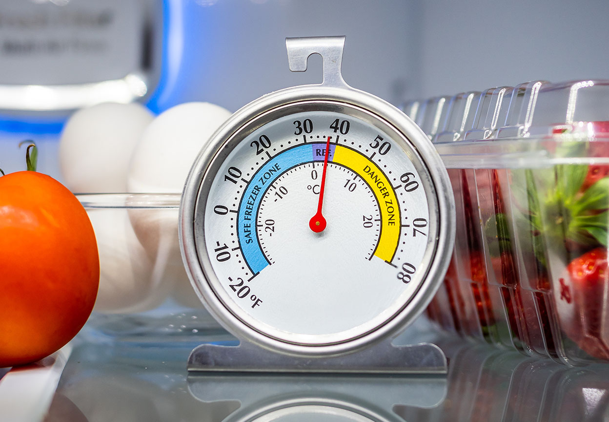 A refrigerator thermometer sits near 40°F on a shelf next to eggs and containers of fresh food
